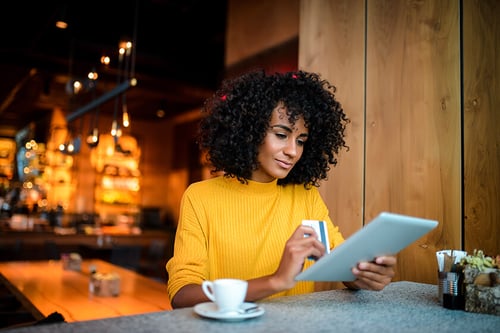 woman at coffeeshop shopping online with her tablet holding a credit card