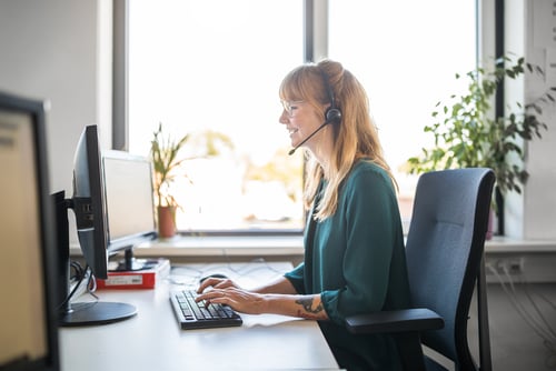 Side view of young female customer service representative using computer at desk in brightly lit office