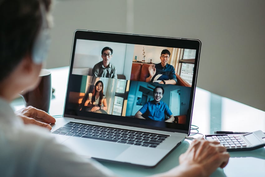 Image of a laptop with a video call open on it and a person blurred out int the background engaging with the call