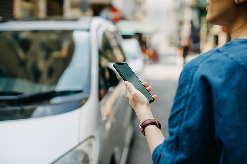 スマートフォンを手に車を見る女性 