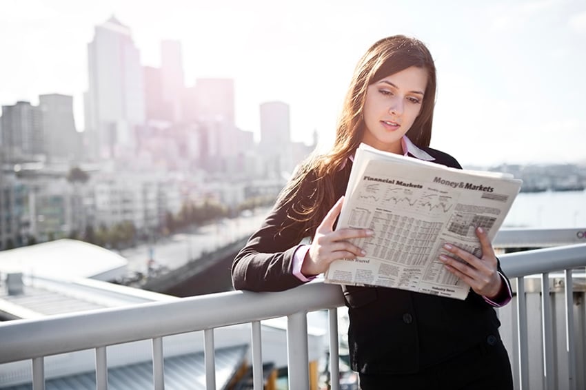 フェンスにもたれて新聞を読む女性