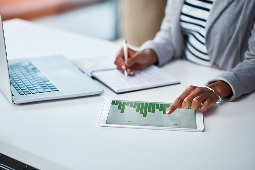 ノートパソコンを前に、金融チャートの情報を書き写す女性