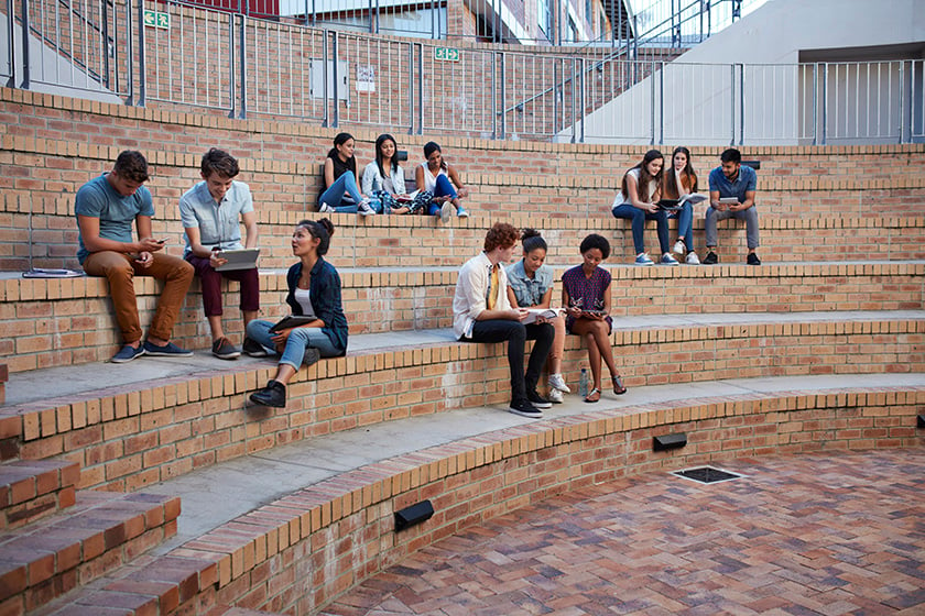 大学内で、青空の下あちこちで集まって勉強をする学生グループ